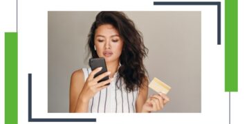 Retrato de una joven y hermosa mujer asiática con tarjeta de crédito, usando su celular con confianza sobre un fondo gris.